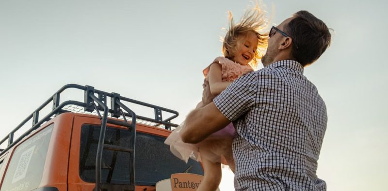 A joyful moment between a father and daughter outdoors with a van in the background.